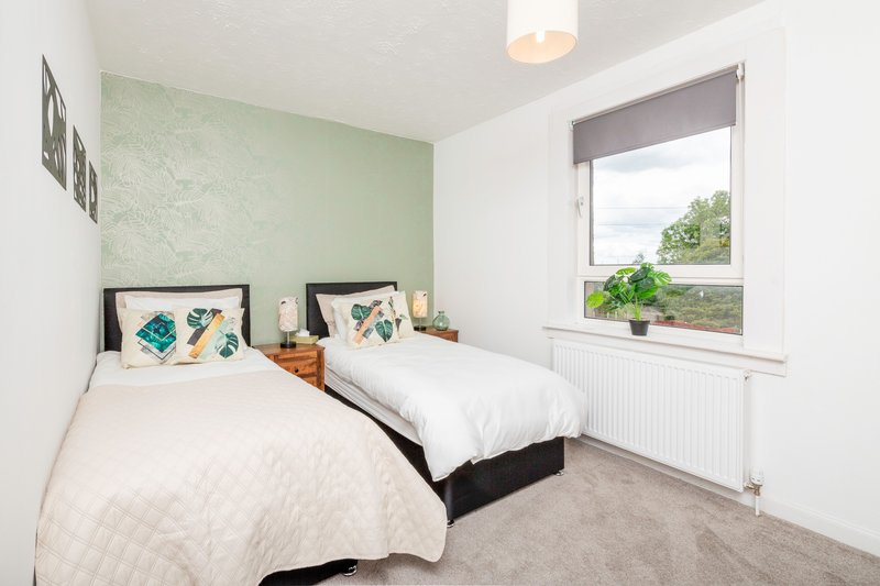 Bright bedroom with two single beds, green accent wall, window with view, and framed artwork