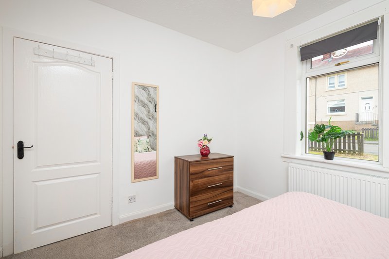 Bright bedroom with pink bedding, wooden chest of drawers, white door and window with street view