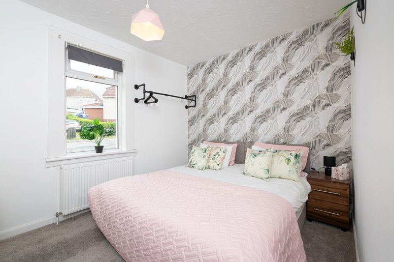 Bedroom with double bed, pink bedding, patterned headboard and window with plants