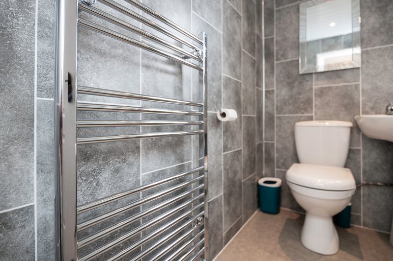 Modern bathroom with heated towel rail, toilet, sink, and grey tile walls