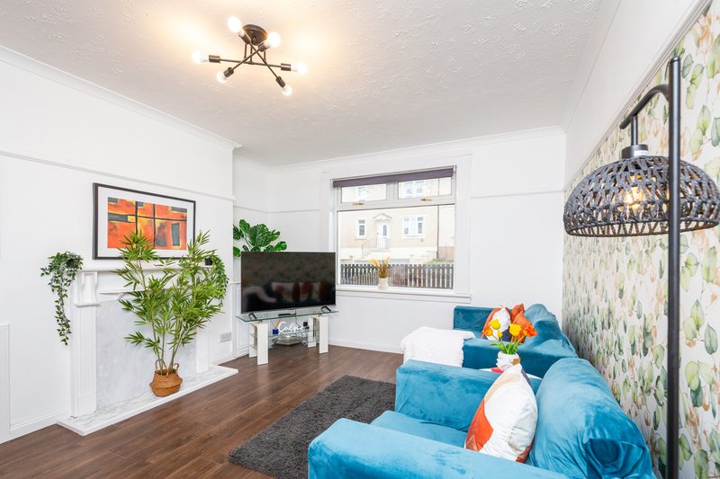 Bright living room with blue sofa, wooden floor, TV, potted plants and window