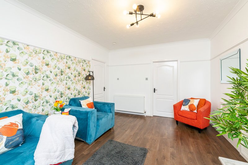Bright living room with blue sofa, orange armchair, patterned wallpaper and wooden flooring