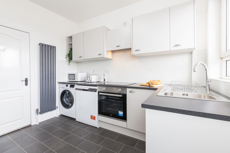 Modern kitchen with white cabinets, black countertop, integrated appliances and washing machine