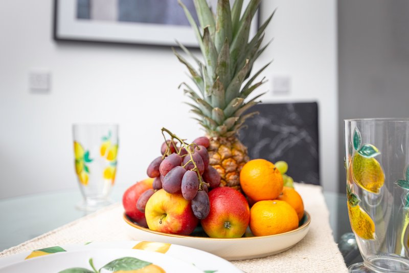 Kitchen counter with fruit bowl containing pineapple, grapes, apples and oranges, decorative glasses