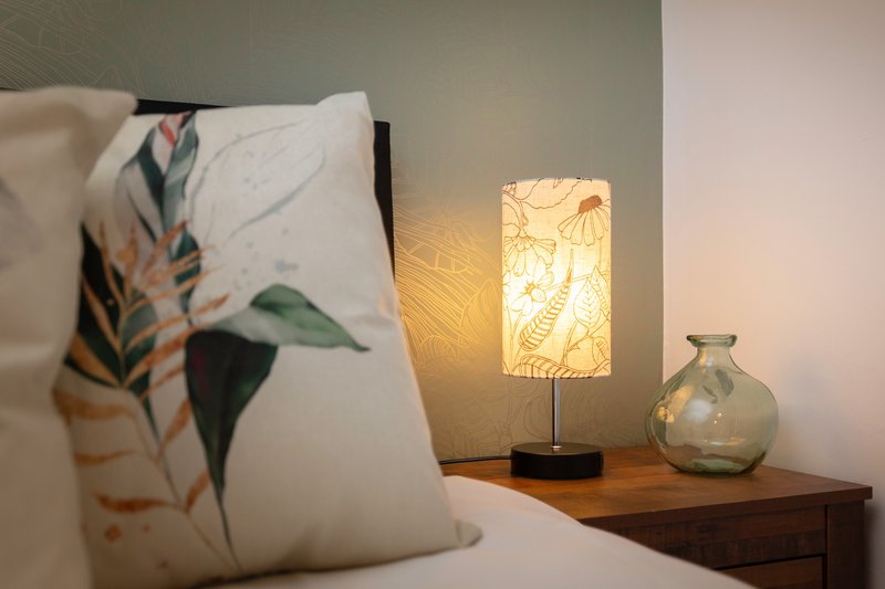 Bedroom nightstand with illuminated lamp, decorative vase, and patterned cushion