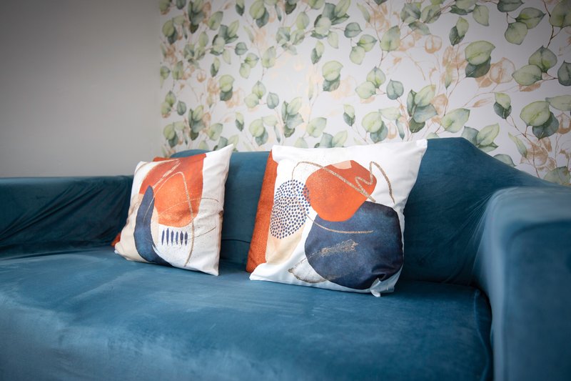 Teal blue sofa with decorative cushions and patterned wallpaper backdrop