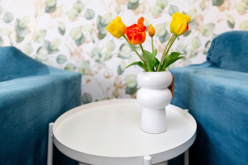 Modern living room with two teal armchairs flanking white side table holding white vase with yellow and red tulips
