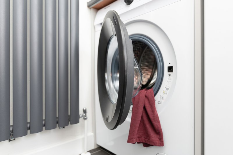 White front-loading washing machine with open door and burgundy towel, grey radiator visible