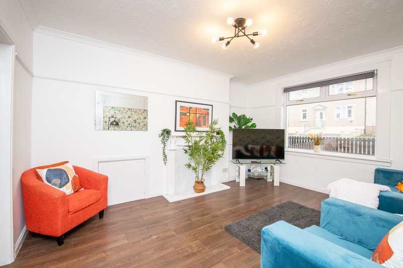 Bright living room with orange armchair, blue sofa, wooden floor and wall art