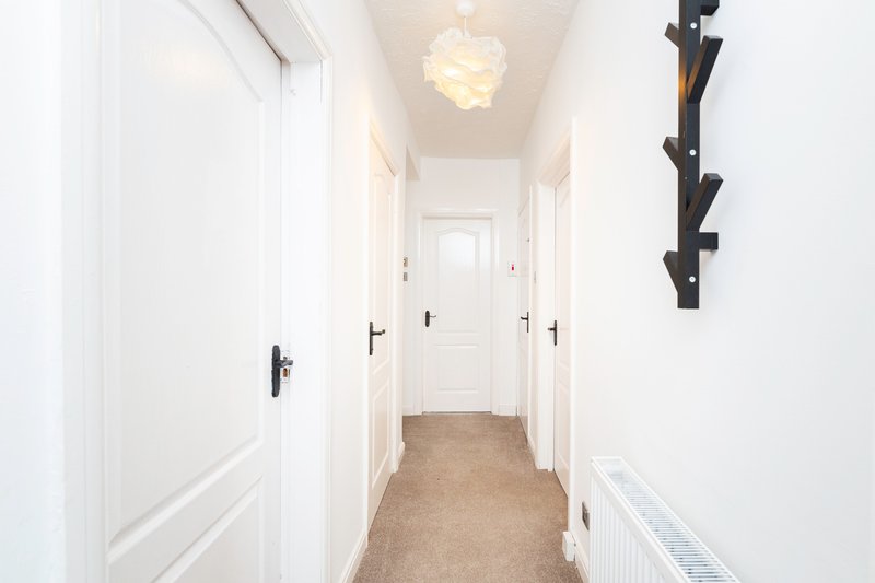 Bright hallway with white doors, pendant light, and beige carpet flooring
