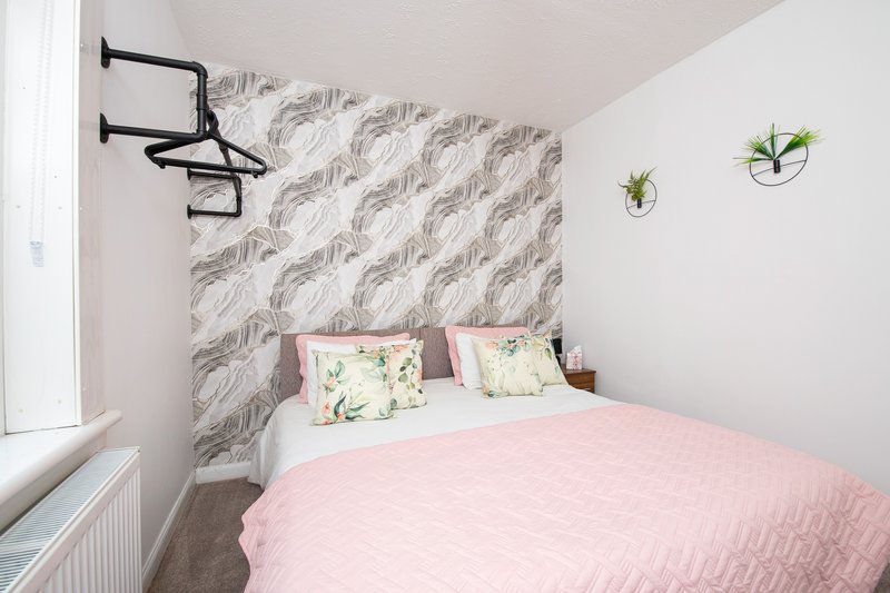 Modern bedroom with pink bedding, patterned headboard wall, wall-mounted shelf and potted plants