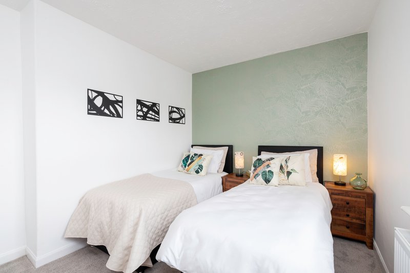 Bedroom with two single beds, wooden bedside tables, green accent wall and wall art