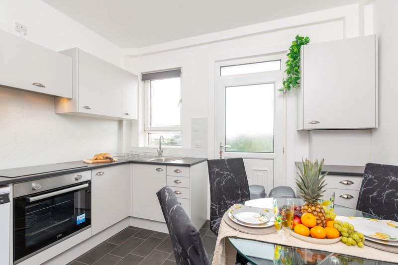 Modern kitchen with white cabinets, black countertops, dining table with place settings and fresh fruit