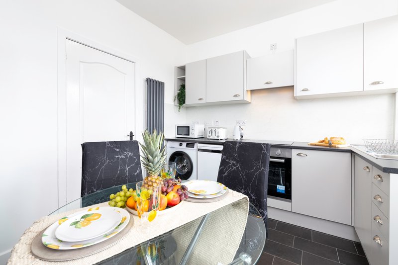 Modern kitchen with dining table, white cabinetry, black countertops and appliances