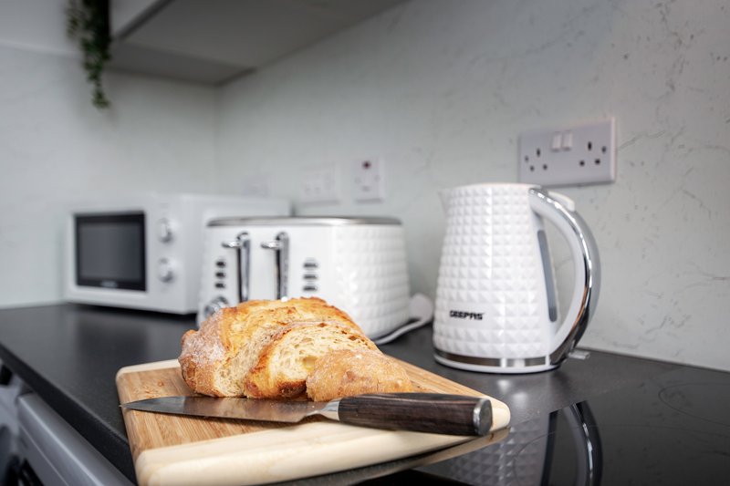 Kitchen countertop with bread, cutting board, kettle, toaster and microwave