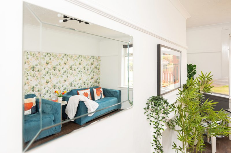 Modern bedroom nook with teal sofa bed, floral headboard, and potted plants by window