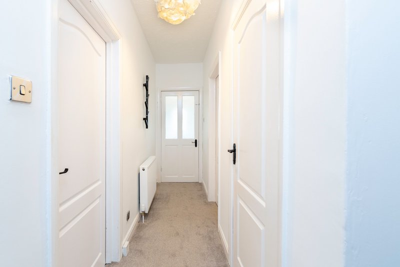 Bright hallway with white doors, pendant light fixture and neutral carpet flooring