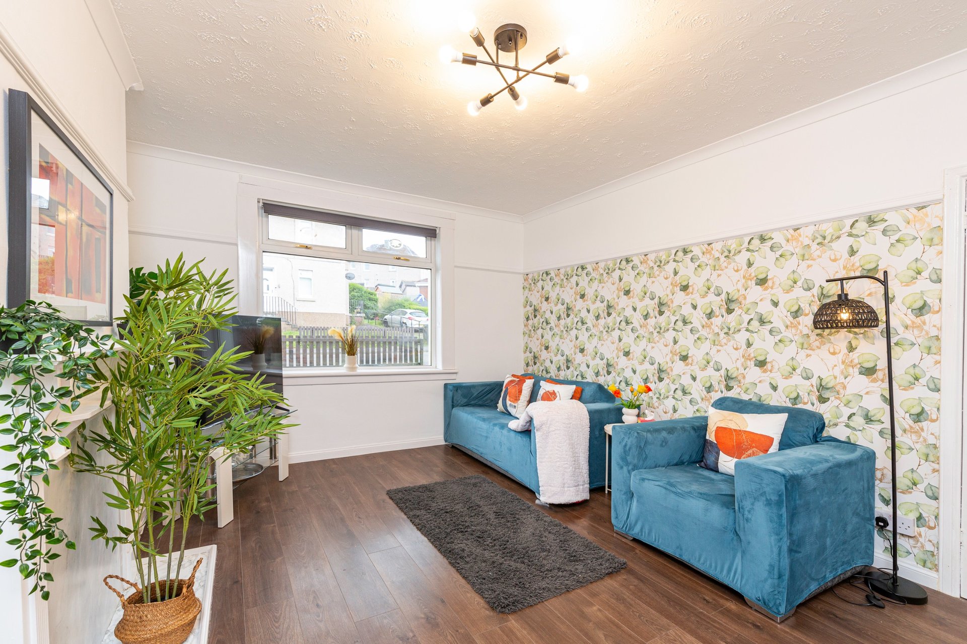 Bright living room with blue sofas, floral wallpaper, potted plants and wooden flooring