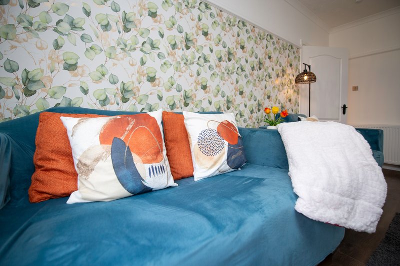 Bedroom with teal bed, orange and white patterned cushions, botanical wallpaper accent wall