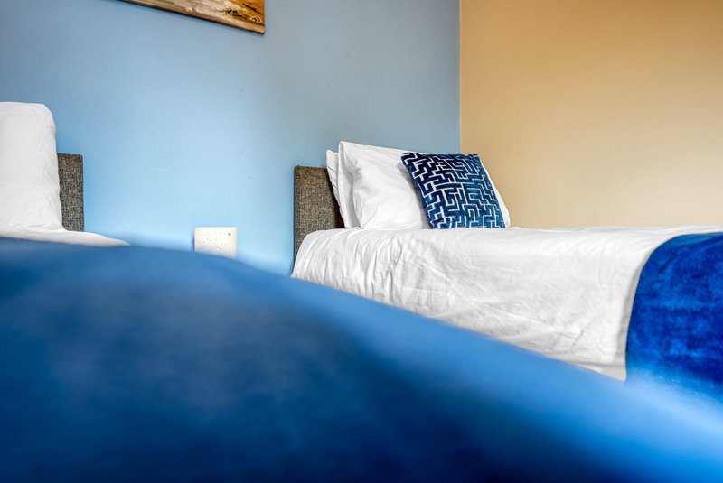 Bedroom with blue bed frame, white pillows, patterned cushion, and neutral walls