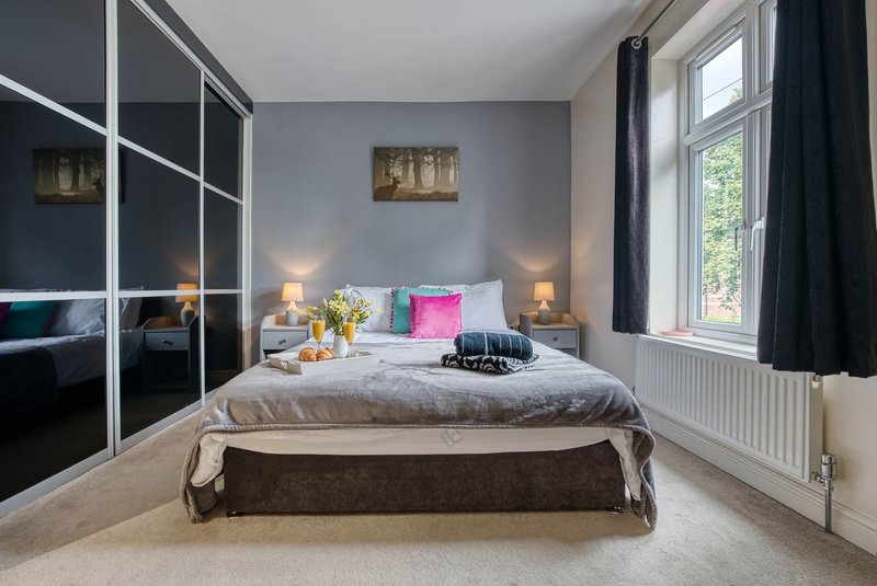 Bright bedroom with double bed, mirrored wardrobe, bedside lamps, and large window