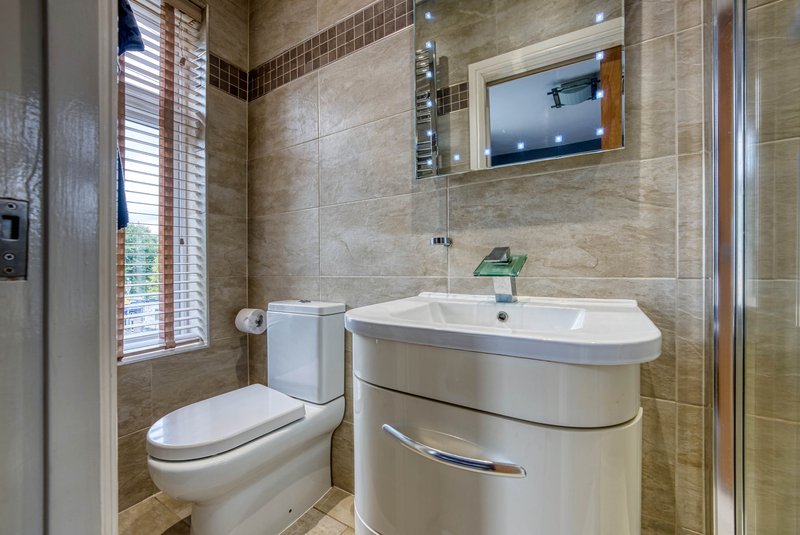 Modern bathroom with curved vanity sink, toilet, mirrored cabinet and tiled walls