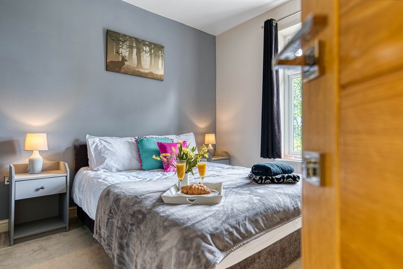 Bright bedroom with double bed, colorful pillows, wooden wardrobe and bedside lamps