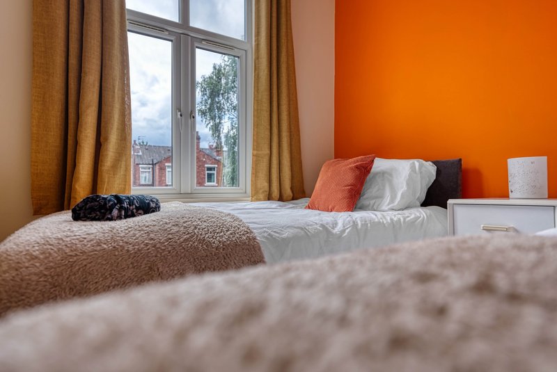 Bedroom with double bed, orange accent wall, window with city view, and cushions