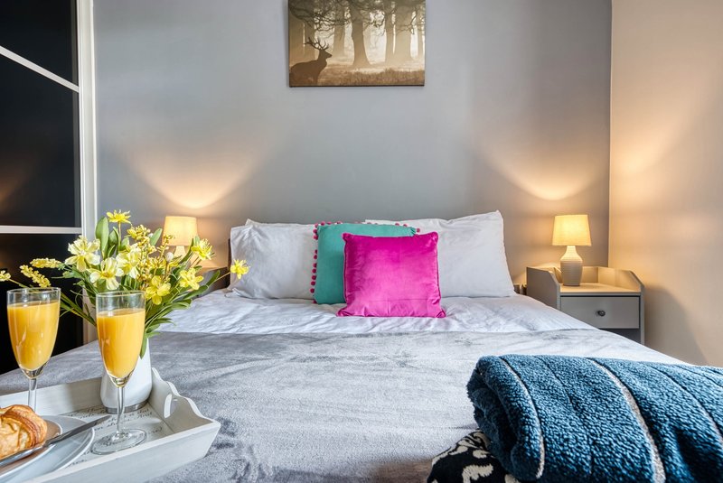 Bright bedroom with queen bed, colorful pillows, bedside lamps, and welcome champagne glasses