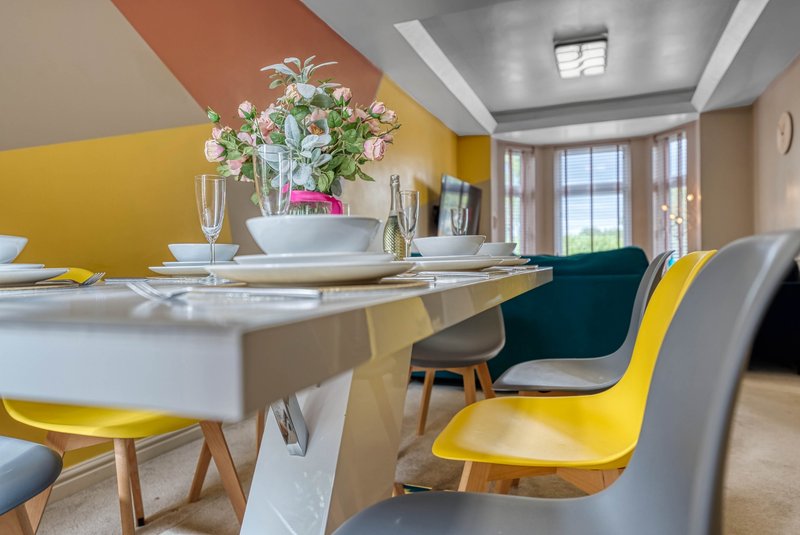Bright dining area with white table, yellow and gray chairs, floral centerpiece and windows