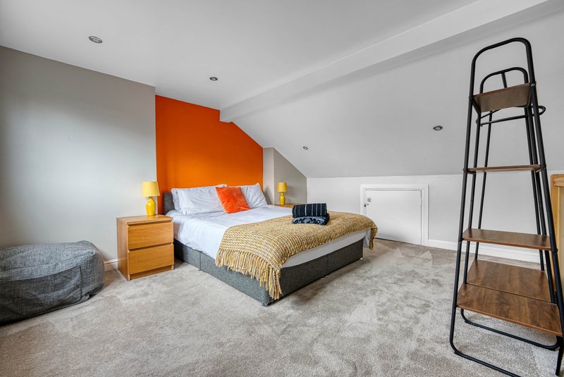 Bright attic bedroom with double bed, orange accent wall, wooden furniture, and sloped ceiling
