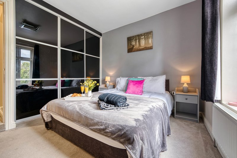 Modern bedroom with double bed, mirrored wardrobe, bedside lamps and framed wall art