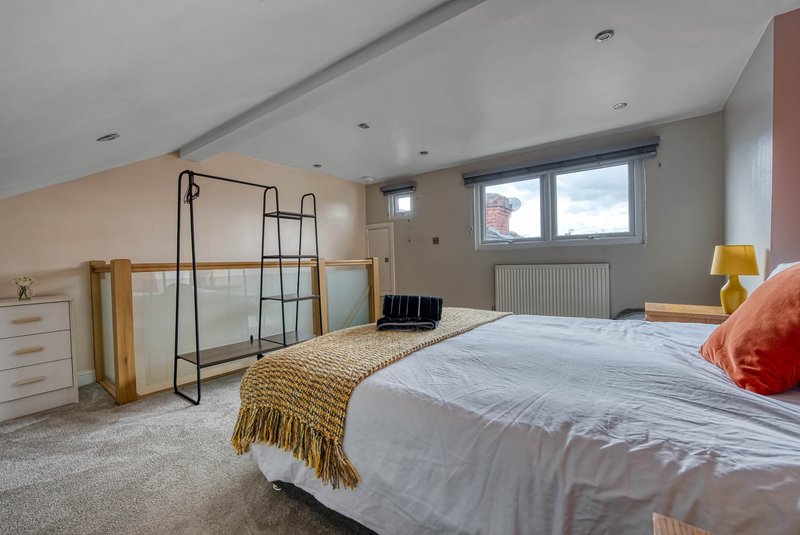 Spacious bedroom with double bed, wooden wardrobe, metal clothing rack and windows