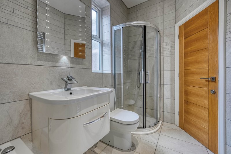 Modern bathroom with white vanity, toilet, curved shower enclosure and wooden door