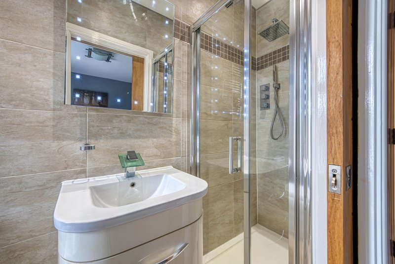 Modern bathroom with curved white sink, large mirror, glass shower enclosure and tile walls