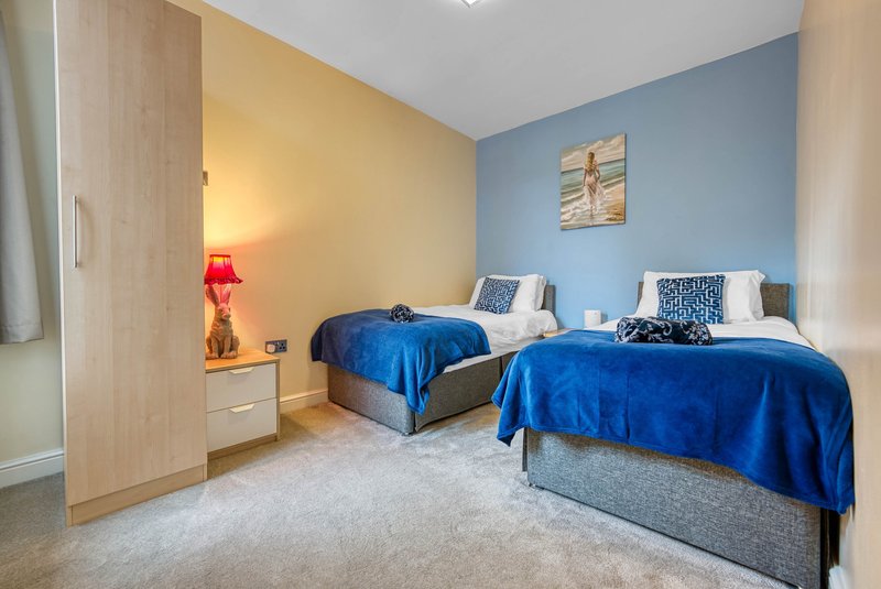Twin bedroom with blue bedspreads, wooden wardrobe, red lamp and light carpeting