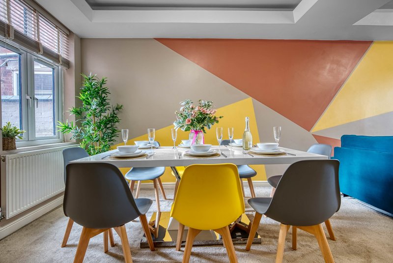 Modern dining room with white table, colorful chairs, geometric wall art, and potted plants