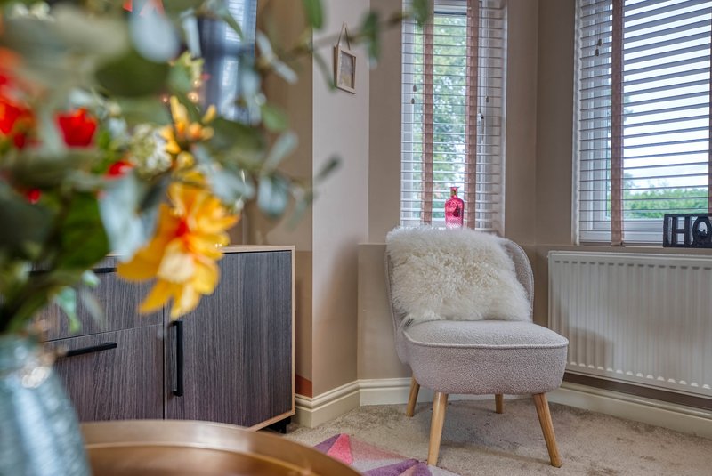Bright living room with cream armchair, wooden cabinet, and window with shutters