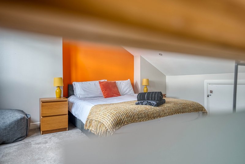 Bright modern bedroom with orange accent wall, double bed, wooden nightstand and warm lighting