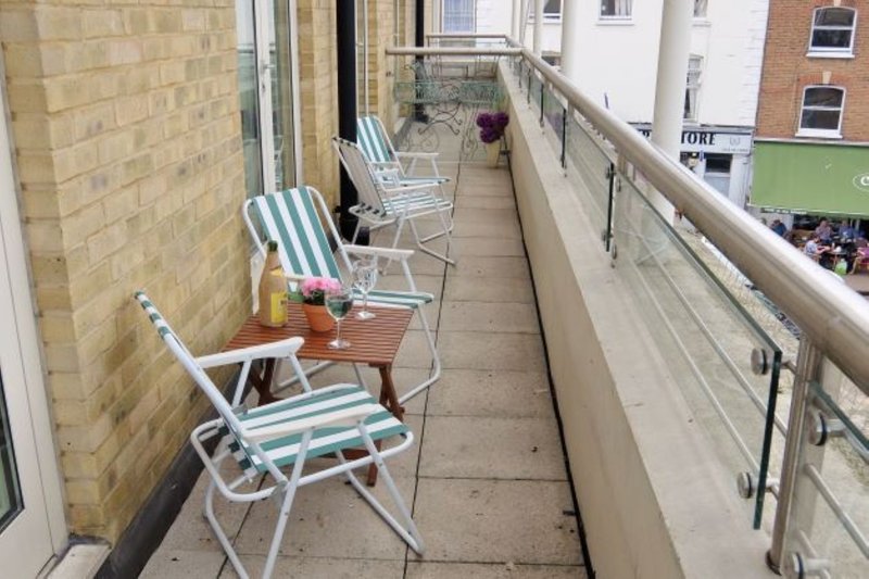 Narrow balcony with striped deck chairs, wooden table, brick wall and metal railing