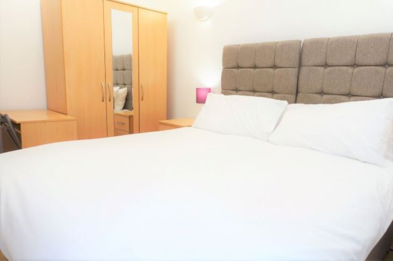 Bedroom with double bed, upholstered headboard, wooden wardrobes and white bedding