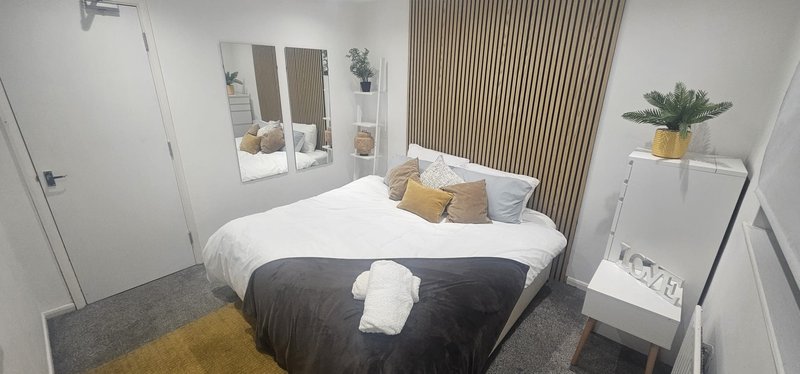 Modern bedroom with double bed, white bedding, yellow and grey accents, mirrored wardrobe