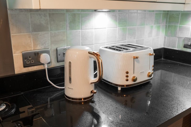 Kitchen counter with cream kettle, toaster, electrical outlets and tiled backsplash