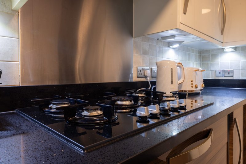Modern kitchen with gas hob, stainless steel splashback, cream units and dark countertop