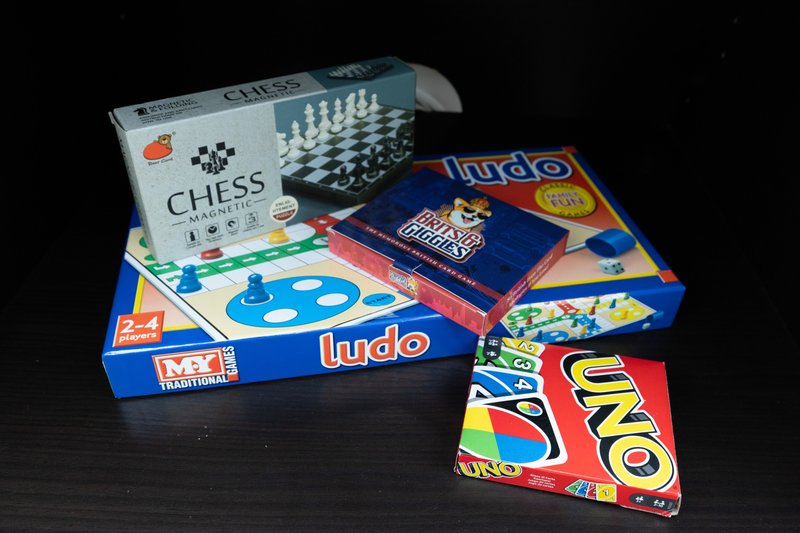 Collection of board games including chess, ludo, and uno stacked on dark surface