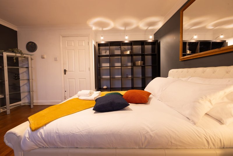 Modern bedroom with white bed, yellow and navy throw pillows, black storage shelves, and pendant lighting