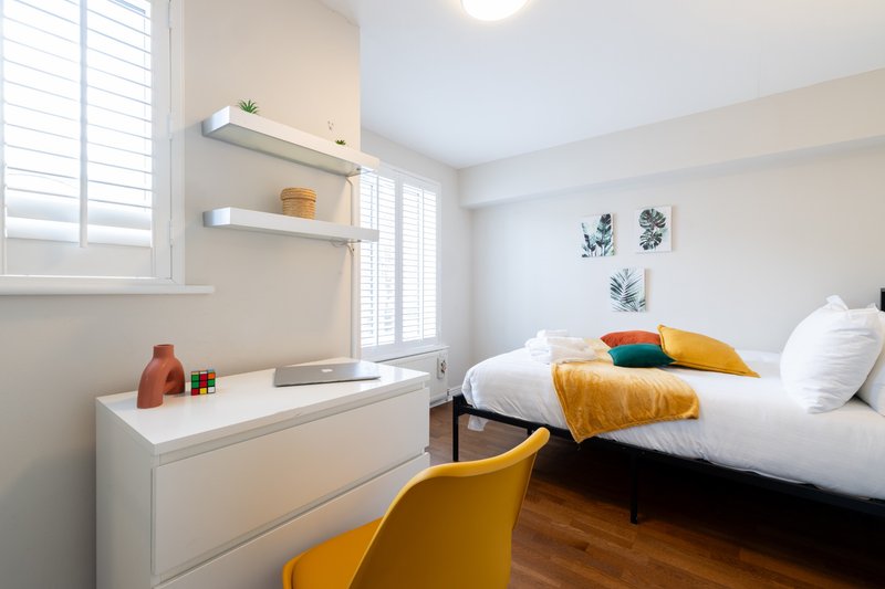 Bright bedroom with double bed, yellow accent chair, white desk, and botanical wall art