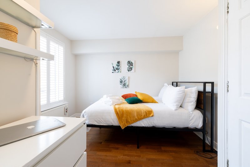 Bright bedroom with double bed, yellow throw, dark wood floor and white walls
