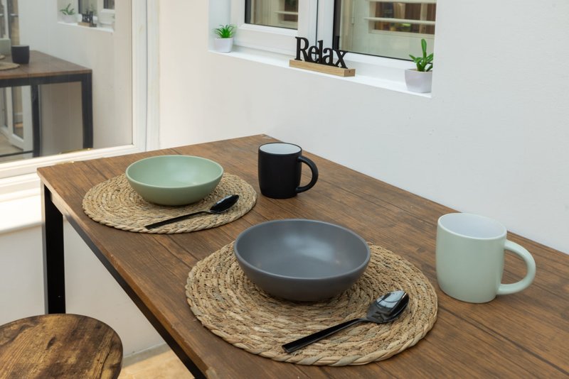 Wooden dining table set with bowls, mugs, placemats and kitchen accessories
