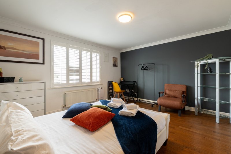 Spacious bedroom with double bed, blue and orange cushions, wooden floor, and armchair